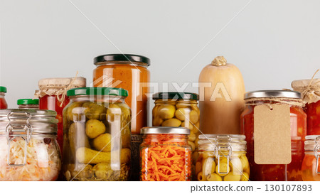 Autumn seasonal pickled or fermented vegetables and mushrooms in jars placed in row on a blue background. Fall home food preserving or canning. Vegetarian and vegan foods, close up 130107893