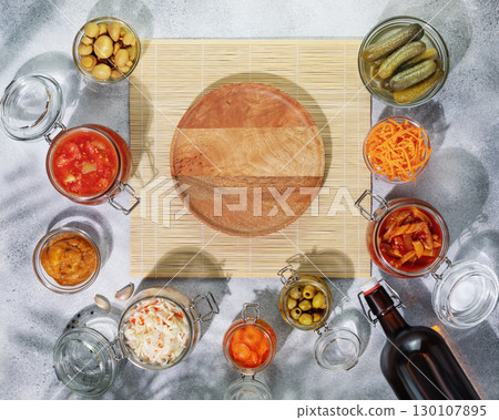 Probiotic food. Pickled or fermented products. Fermented vegetables and mushrooms in glass jars, bottle with home made beer around empty wooden plate on a natural mat. Home food preserving or canning Probiotic food. Pickled or fermented products. Fermented vegetables and mushrooms in glass jars, bottle with home made beer around empty wooden plate on a natural mat. Home food preserving or canning 130107895