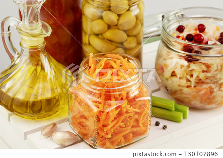Autumn seasonal pickled or fermented vegetables, mushrooms and olive oil in glass jars on a white wooden board on a light neutral background with garlic. Fall home food preserving or canning. Close up 130107896