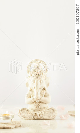 Holiday of Ganesh Chaturthi. Sculpture of ganesha with rose petals and candles on a light background with copy space. Healing health and energy, relaxing. Soft focus style, smartphone format Holiday of Ganesh Chaturthi. Sculpture of ganesha with rose petals and candles on a light background with copy space. Healing health and energy, relaxing. Soft focus style, smartphone format 130107897