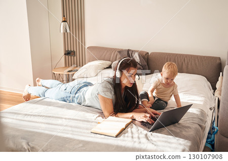 On the comfortable bed. Mother with her little son is at home in domestic room On the comfortable bed. Mother with her little son is at home in domestic room 130107908