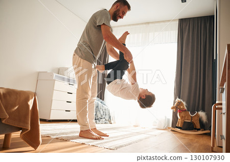 Playing, holding in hands. Man is playing with his little son in the domestic room 130107930