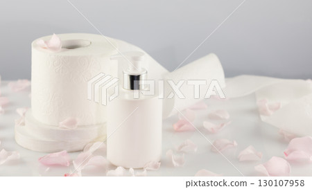 Roll of toilet paper with cosmetic dispenser bottle on light background with rose petals and copy space. White toilet tissue, Hygiene product. Restroom soft touch toilet paper. Soft focus style image Roll of toilet paper with cosmetic dispenser bottle on light background with rose petals and copy space. White toilet tissue, Hygiene product. Restroom soft touch toilet paper. Soft focus style image 130107958