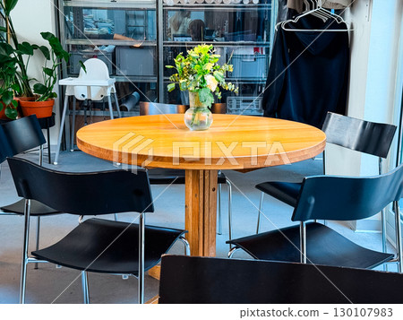 Round wooden table with vase of flowers inside cafe. Interior design, lifestyle, and social gathering. 130107983