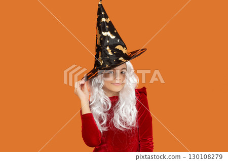 Happy Halloween. Girl witch in Halloween costume isolated on orange. Trick or treat. All Hallows costume party celebration. All Hallows witch. Girl in Halloween witch costume. Enchanting gaze Happy Halloween. Girl witch in Halloween costume isolated on orange. Trick or treat. All Hallows costume party celebration. All Hallows witch. Girl in Halloween witch costume. Enchanting gaze 130108279
