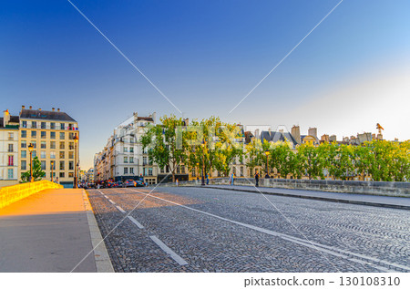 Pont Marie bridge cobblestone street road to Saint-Louis island in Paris historic city center with old typical buildings, blue sky background, France 130108310