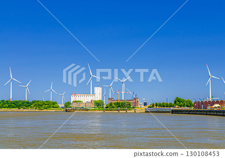 Landscape of Scheldt river and Linkeroever Left bank of Antwerp with Windmill farm wind power plant turbines on horizon, Antwerpen port area, Flemish Region, Belgium 130108453
