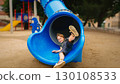 Happy Child Playing on Blue Slide in Playground 130108533