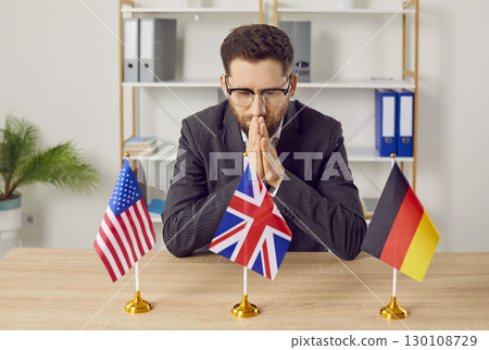 Young man sitting at desk in office with USA, Great Britain and Germany flags. 130108729