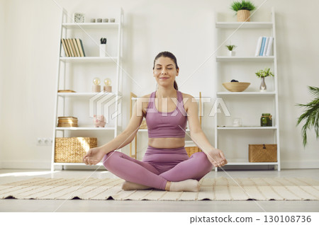 Portrait of a relaxed young woman doing yoga exercise at home sitting in lotus pose. Portrait of a relaxed young woman doing yoga exercise at home sitting in lotus pose. 130108736