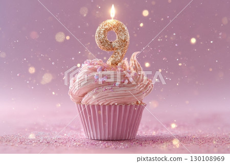 A pink cupcake with a lit candle shaped like the number nine and colorful sprinkles on top. Festive defocused bokeh background 130108969