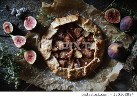 A rustic galette with fresh figs and herbs on parchment paper. A rustic galette with fresh figs and herbs on parchment paper. 130108984