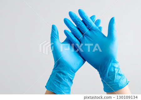 Two hands wearing blue latex gloves held up against a light gray background. 130109134