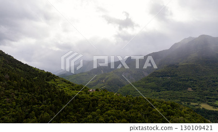 Dark green forested slopes lead to misty mountain peaks in the French Alps, creating a dramatic and moody landscape Dark green forested slopes lead to misty mountain peaks in the French Alps, creating a dramatic and moody landscape 130109421