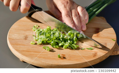 chef cuts fresh green onion on cutting board 130109442