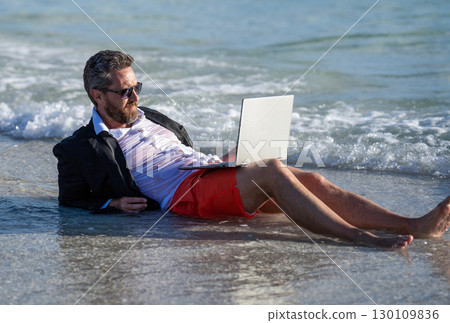 Summer business. Businessman relaxing at the beach. businessman relax at beach. businessman in suit with laptop in summer. Businessman dreams on summer business in sea. recharge through travel Summer business. Businessman relaxing at the beach. businessman relax at beach. businessman in suit with laptop in summer. Businessman dreams on summer business in sea. recharge through travel 130109836