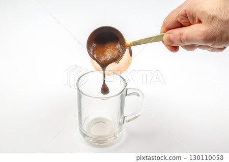 The process of pouring Turkish coffee from a classic cezve into a clear cup 130110058
