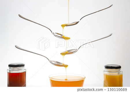 Fresh flower honey drips from a spoon into a spoon on a white background. Organic vitamin food. 130110089