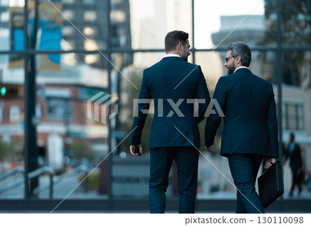 Two businessmen in elegant business suit. Business center. Walking colleague. Colleague and friends. Two successful business men walking outdoor. Businessmen go to work. Business talking 130110098