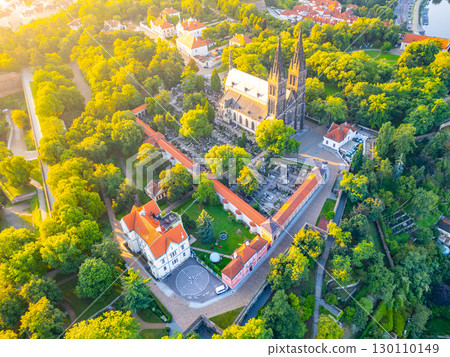 The Basilica of St. Peter and St. Paul stands majestically in Vysehrad, Prague, surrounded by lush greenery as the morning sun bathes the area in warm light, creating a serene atmosphere. The Basilica of St. Peter and St. Paul stands majestically in Vysehrad, Prague, surrounded by lush greenery as the morning sun bathes the area in warm light, creating a serene atmosphere. 130110149
