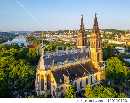 Golden morning light bathes the Vysehrad Basilica of St. Peter and St. Paul in Prague. Surrounded by greenery, the cathedral stands tall against the skyline, reflecting a tranquil moment of the dawn. Golden morning light bathes the Vysehrad Basilica of St. Peter and St. Paul in Prague. Surrounded by greenery, the cathedral stands tall against the skyline, reflecting a tranquil moment of the dawn. 130110150