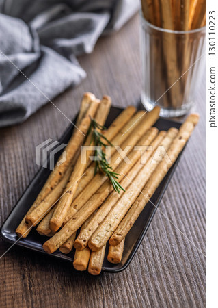 Crispy grissini breadsticks on plate on wooden table. 130110223