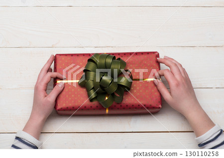 Female hands hold box wrapped in red paper with bow. Female hands hold box wrapped in red paper with bow. 130110258