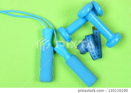 Dumbbells and jump rope in cyan color on green background Dumbbells and jump rope in cyan color on green background 130110290