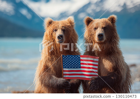 Two grizzly bears hold a US flag in their paws while standing against a backdrop of mountains and nature. Mountains and steppes in the background. 130110473