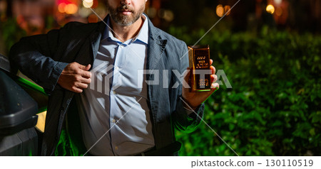Business success gold bar. Investment in precious metal. Golden bullion. Golden bar. Rich businessman hold gold bullion at night, cropped view. Financial success. Successful rich man with gold 130110519
