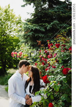 Young loving married couple embracing in a garden surrounded by vibrant red roses and greenery Young loving married couple embracing in a garden surrounded by vibrant red roses and greenery 130110551