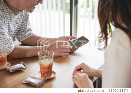 男人和女人一邊看著智慧型手機一邊微笑著交談 130111174