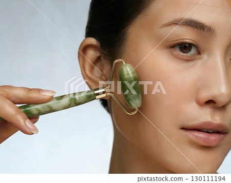 Woman using jade stone jade roller for facial massage beauty wellness skincare and rejuvenating natural selfcare treatment 130111194