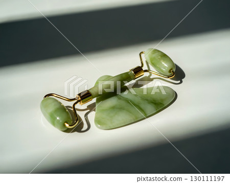 Jade roller and gua sha set on white surface sunlight for beauty wellness skincare facial massage and natural woman selfcare 130111197