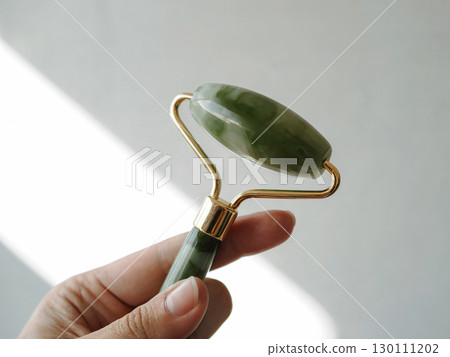 Close-up woman hand holding jade stone jade roller for skincare wellness beauty facial massage and natural rejuvenation 130111202