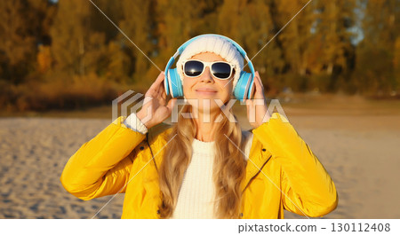 Happy young woman enjoying listening to music in headphones outdoors on autumn beach Happy young woman enjoying listening to music in headphones outdoors on autumn beach 130112408