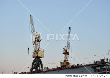 Industrial Cranes Skillfully Operating at Dusk Within a Busy and Vibrant Shipyard Environment 130112576