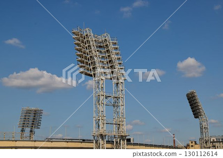 The illuminated floodlights of the sports stadium shine brightly against the clear sky The illuminated floodlights of the sports stadium shine brightly against the clear sky 130112614