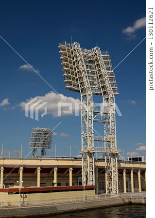 Floodlights shining bright at a historic stadium under a beautiful blue sky stretching above 130112621