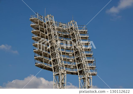 An Illuminated Sports Facility Lighting Tower Is Set Under a Clear Blue Sky Above Us An Illuminated Sports Facility Lighting Tower Is Set Under a Clear Blue Sky Above Us 130112622