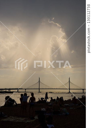 Sunbeams gently break through fluffy clouds above the serene beach and a beautiful bridge 130112738