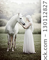 Fantasy landscape of a woman in a white dress touching a unicorn in the forest 130112827