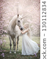 Fantasy landscape of a woman in a white dress touching a unicorn 130112834