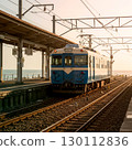 A blue and white train stopping at a station overlooking the sea 130112836