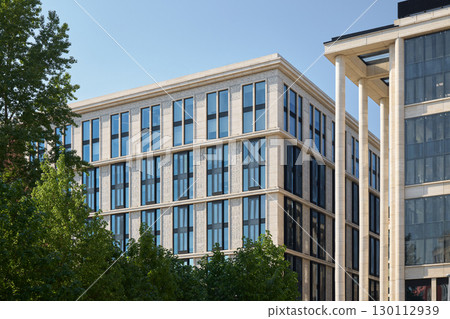 A modern urban building with a sleek glass facade in vibrant green surroundings A modern urban building with a sleek glass facade in vibrant green surroundings 130112939