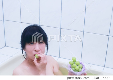 一位年輕女子一邊洗澡一邊吃著陽光麝香葡萄 一位年輕女子一邊洗澡一邊吃著陽光麝香葡萄 130113642
