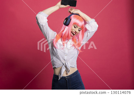 Attractive young lady filled with excitement, singing and dancing with her arms raised against isolated background. Beautiful female music lover wearing wireless headphones, enjoying song playlist. 130114076