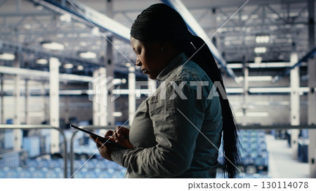 IT expert monitors server farm activity using tablet while walking on industrial platform. Data center system administrator reviews rigs tests results to ensure systems are working correctly, camera B IT expert monitors server farm activity using tablet while walking on industrial platform. Data center system administrator reviews rigs tests results to ensure systems are working correctly, camera B 130114078