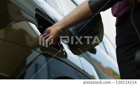 Close up of driver disconnecting EV vehicle from charging dock, concept of low carbon footprint commitment. Man unplugging electric car from power supply after recharge, low angle shot 130114214