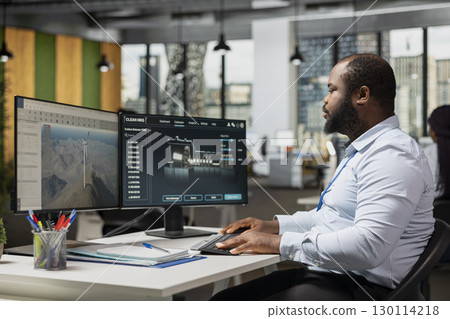 Engineer in office uses dual monitor setup to analyze turbine mechanics and windmill farm layouts. Researcher calibrates turbine components for higher efficiency and lower environmental impact Engineer in office uses dual monitor setup to analyze turbine mechanics and windmill farm layouts. Researcher calibrates turbine components for higher efficiency and lower environmental impact 130114218